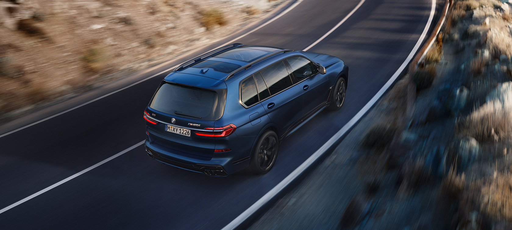 BWM X7 M60i xDrive G07 LCI Frozen Marina Bay Blue вид ззаду в три чверті водіння BWM X7 M60i xDrive G07 LCI Frozen Marina Bay Blue вид ззаду в три чверті водіння вулицею з висоти пташиного польоту