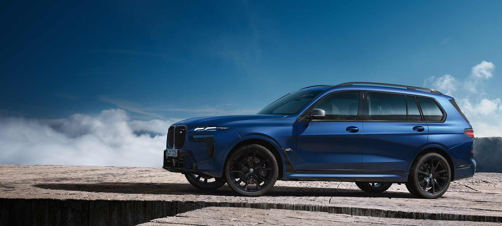 BWM X7 M60i xDrive G07 LCI Frozen Marina Bay Blue вид збоку на місці перед гірським пейзажем