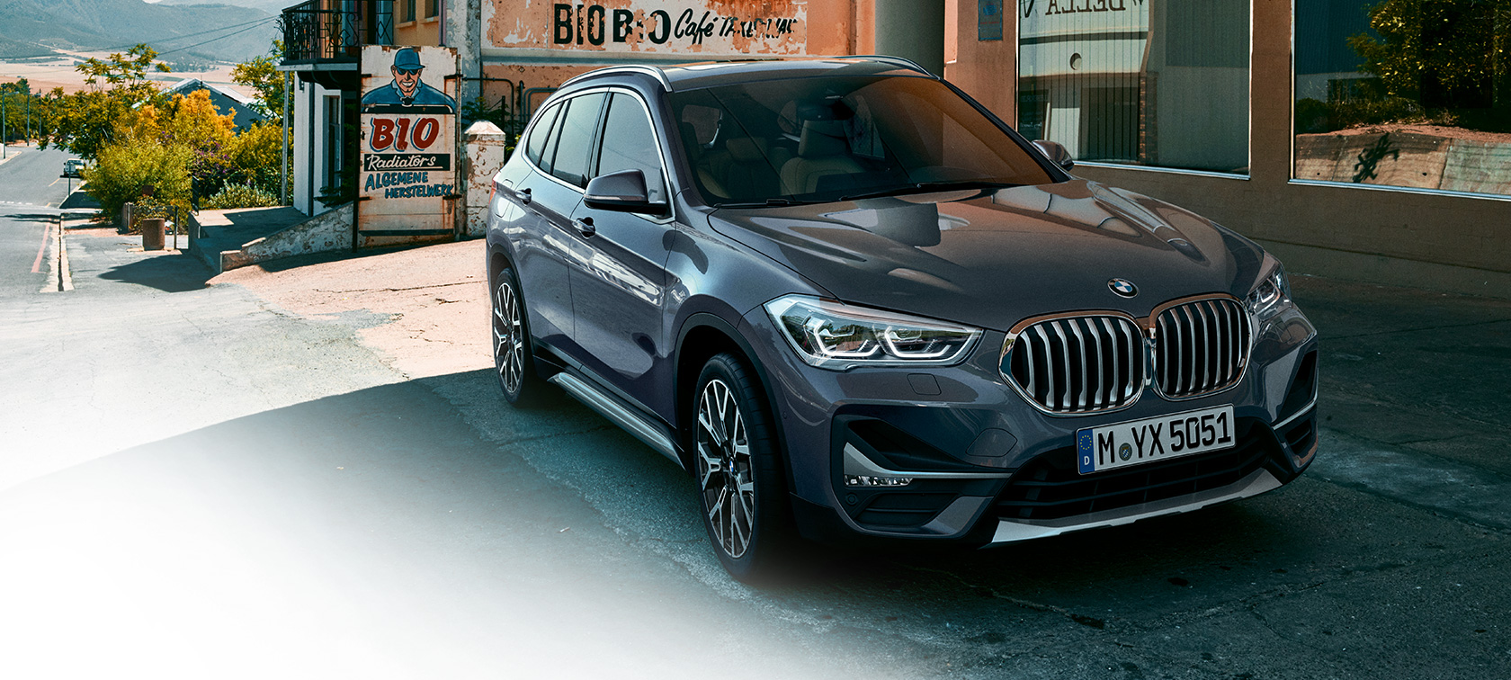 BMW X1, вид спереди с поворотом в три четверти. BMW X1, вид спереди с поворотом в три четверти на фоне городского пейзажа.