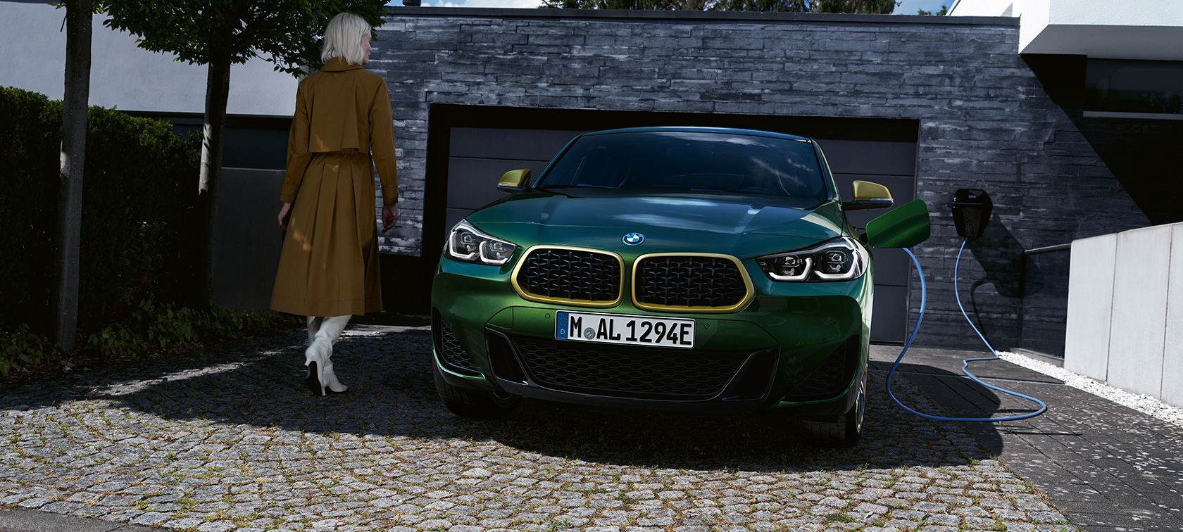 Вид спереду на BMW Х2 F39 у кольорі Sanremo Green metallic Вид спереду під час зарядки з моделлю зліва BMW X2 F39 у кольорі Sanremo Green metallic