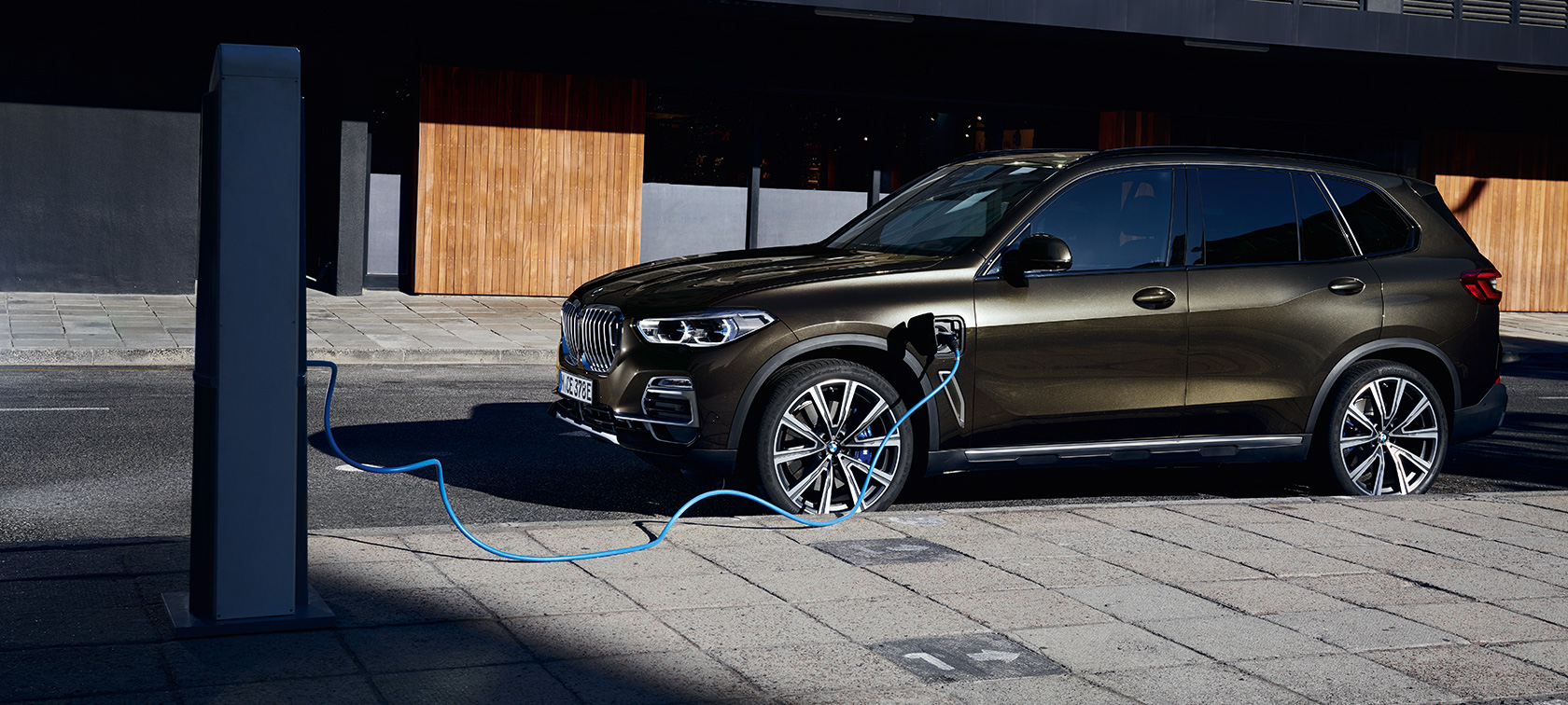 Плагін-гібрид BMW X5 xDrive45e G05 вид три чверті збоку Плагін-гібрид BMW X5 xDrive45e G05, вид на машину збоку під час заряджання
