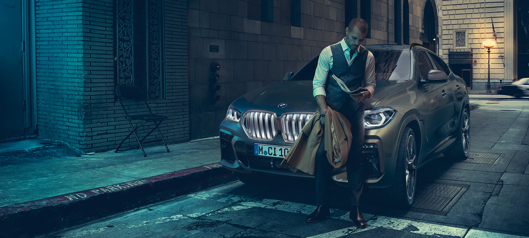 Людина спирається на BMW X6. Чоловік спирається на BMW X6 в бічній перспективі перед міською обстановкою.