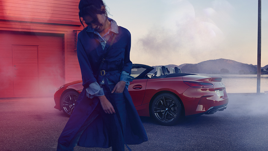 BMW Z4 M40i Roadster G29 з відкритим дахом BMW Z4 M40i Roadster G29 вид ззаду з поворотом у три чверті з відкритим дахом та жінкою на передньому плані