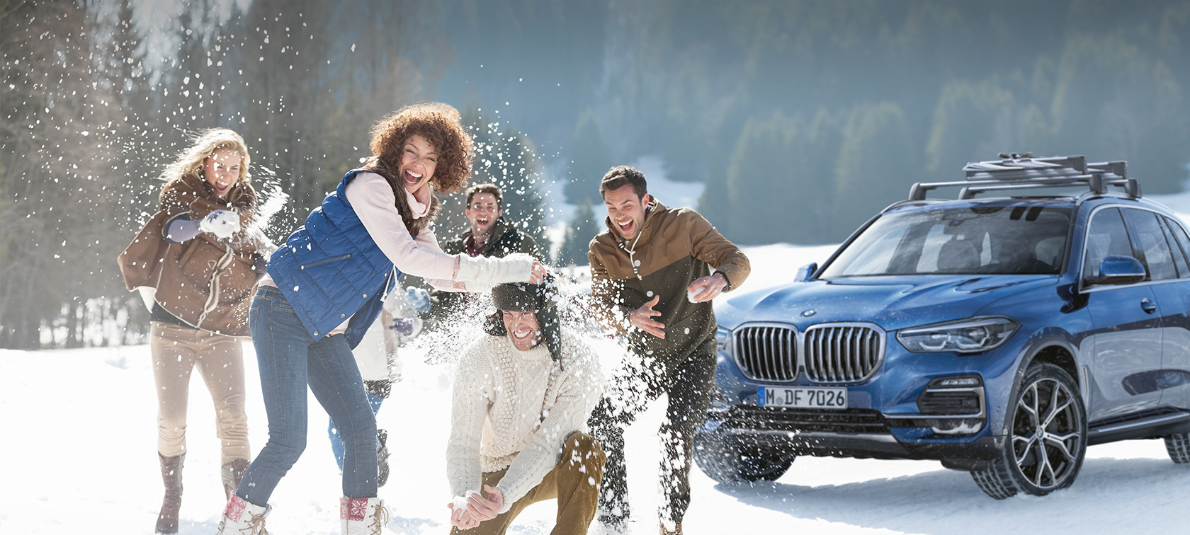 Оригінальні аксесуари та сервіс BMW для осені та зими Жінки та чоловіки сміються на снігу перед BMW