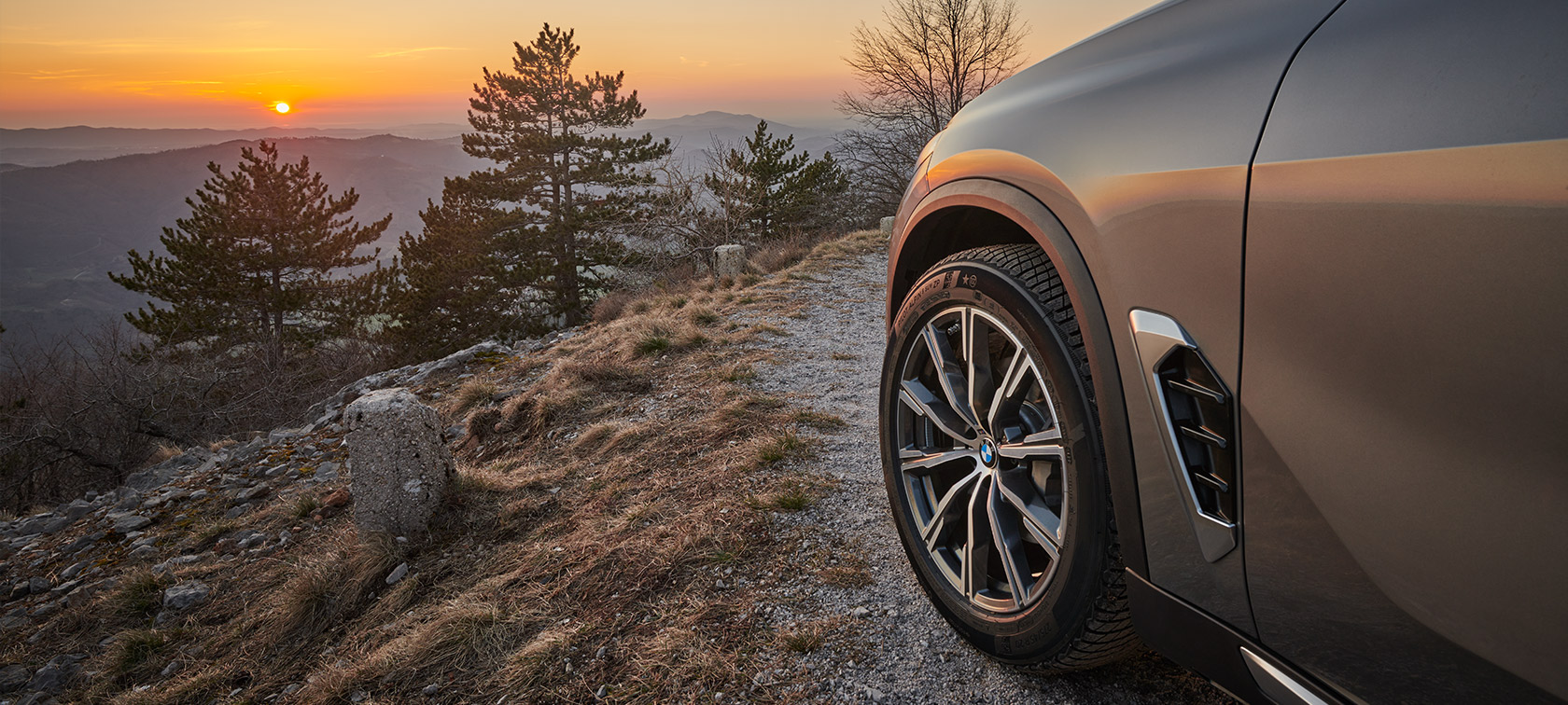 Оригінальні колісні диски BMW на BMW X5 (G05 LCI) на ґрунтовій дорозі на схилі гори, з видом на захід сонця Оригінальні колісні диски BMW на BMW X5 (G05 LCI)