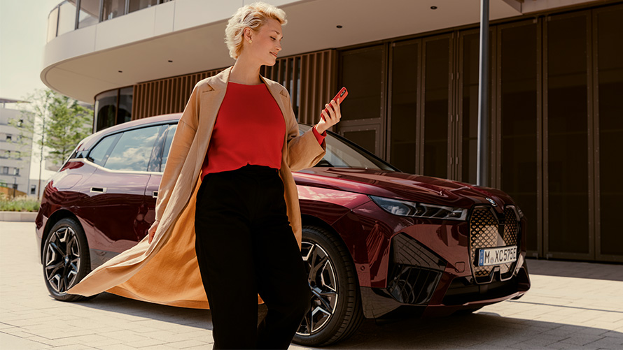 Застосунок My BMW, жінка зі смартфоном перед автомобілем BMW Жінка зі смартфоном стоїть перед BMW